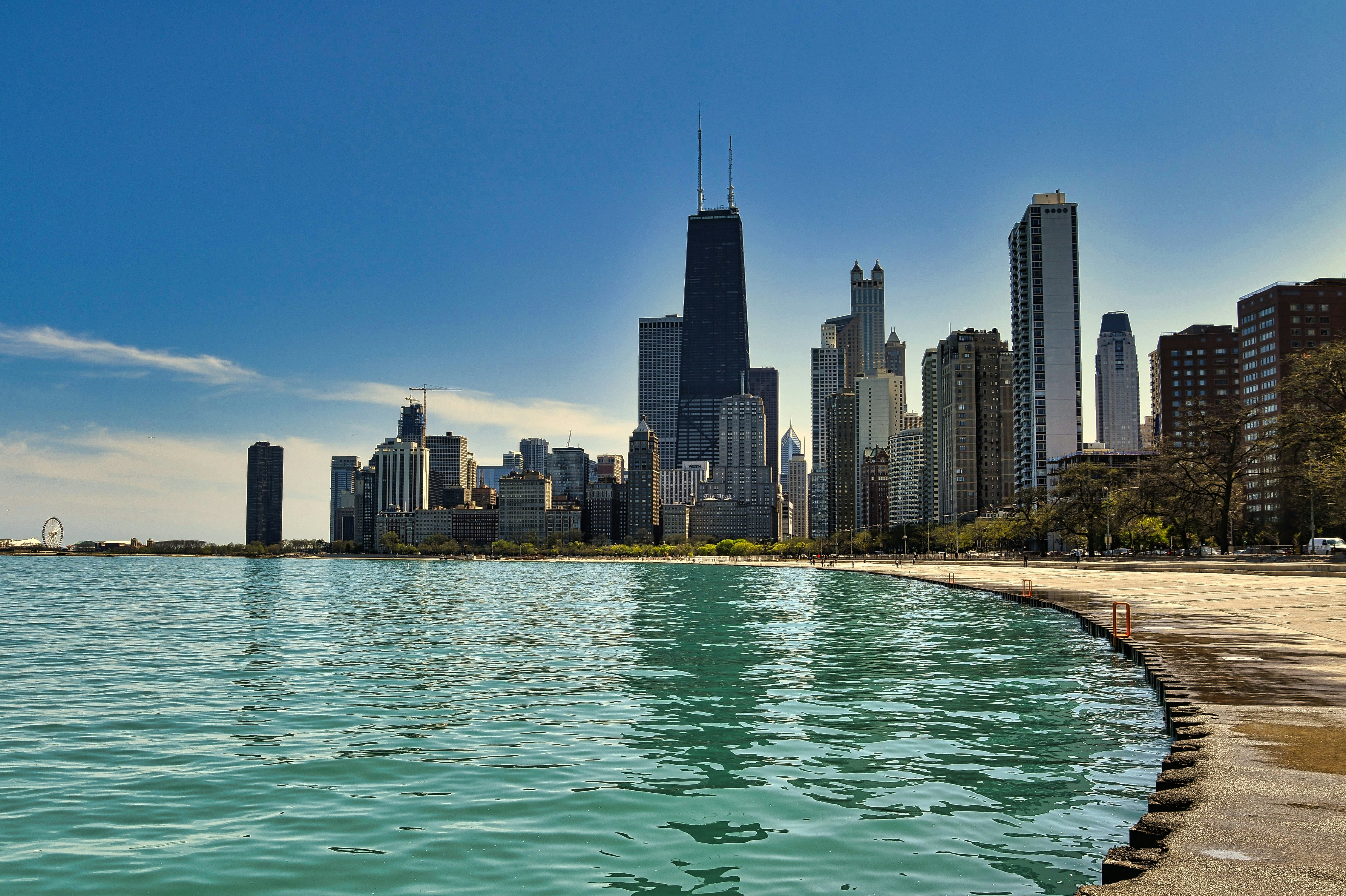 A panoramic view of the Chicago skyline along the waterfront, showcasing tall skyscrapers against a clear blue sky and the shimmering water of Lake Michigan.