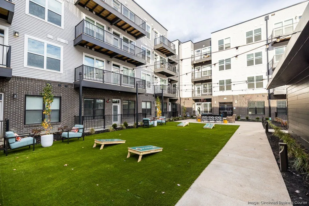 A well-maintained green outdoor area within an apartment complex, featuring lawn, seating areas, and corn hole games.