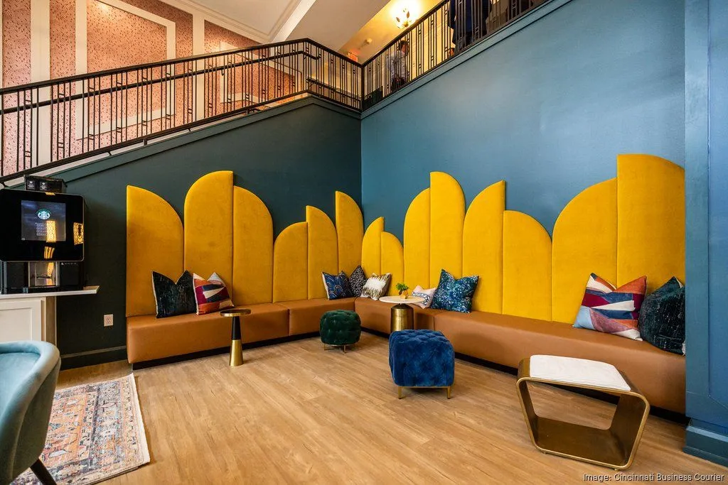 A modern community lounge space featuring bright yellow seating along a blue wall with a staircase in the background.