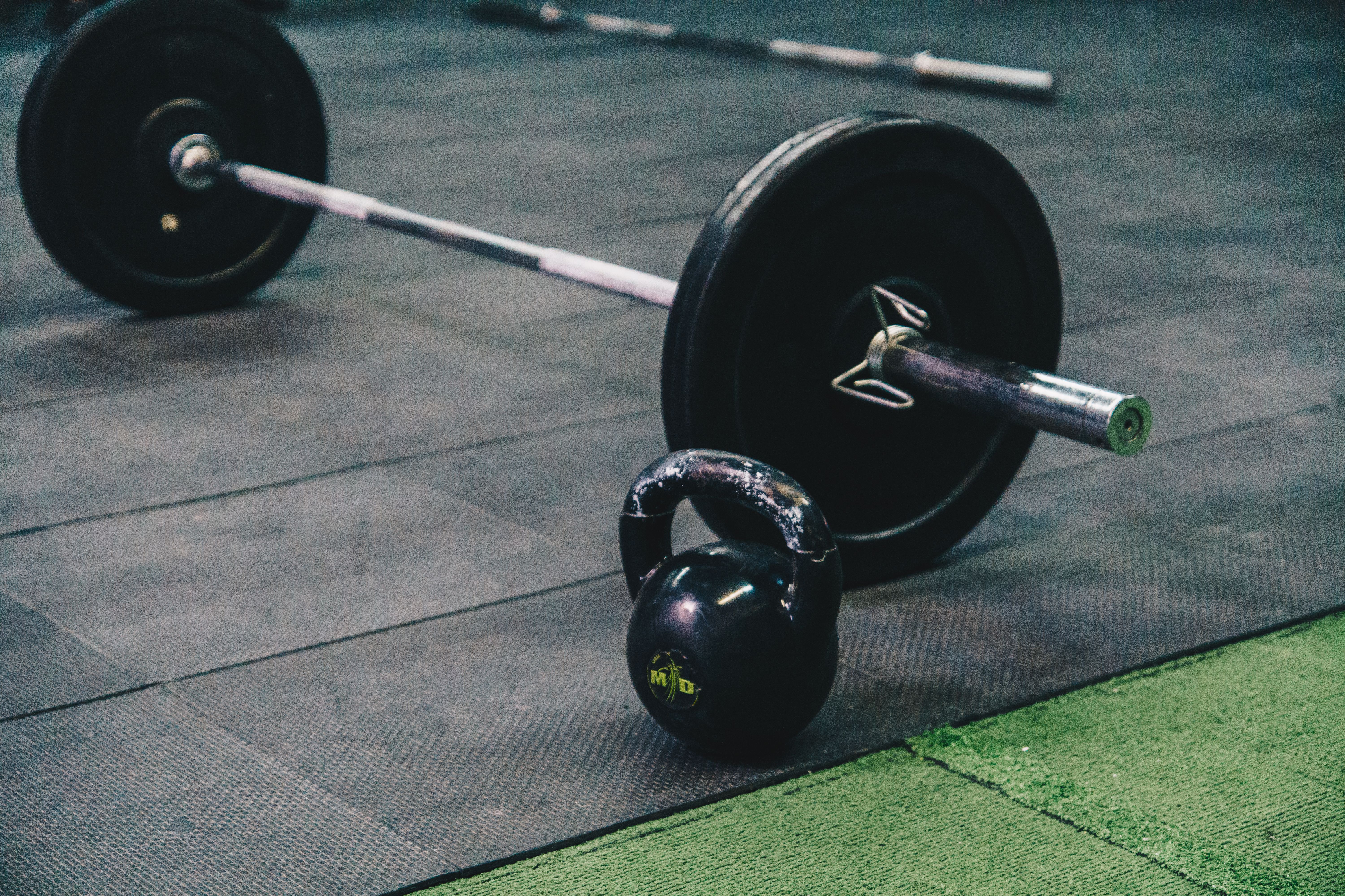 A barbell and a kettlebell on gym flooring.