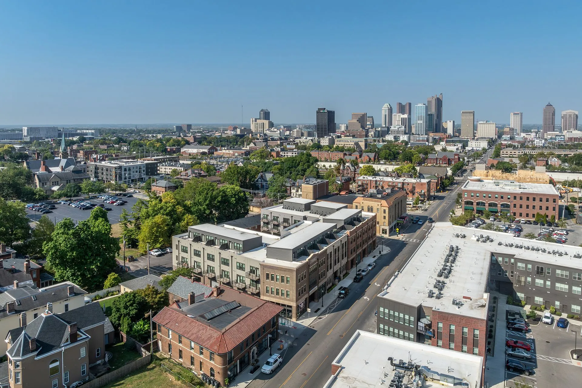 A panoramic view of a city skyline featuring a mix of modern and historic buildings, greenery, and streets bustling with houses and shops.
