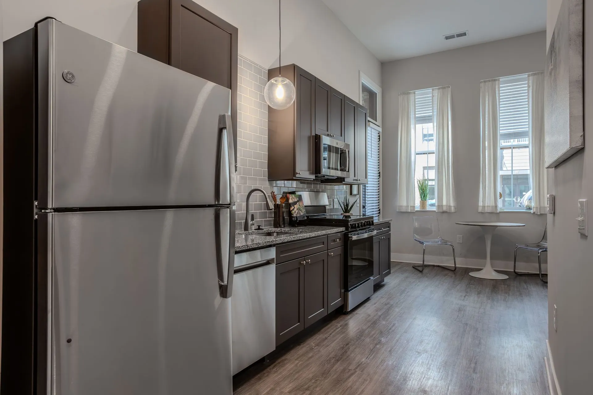 A modern kitchen featuring stainless steel appliances, dark wood cabinets, and a small dining area with two chairs and a round table by the windows.