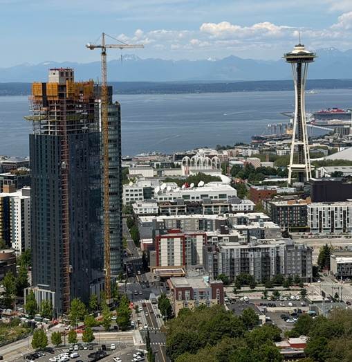 An aerial view of Seattle featuring a construction site next to a tall completed building and the iconic Space Needle in the background.