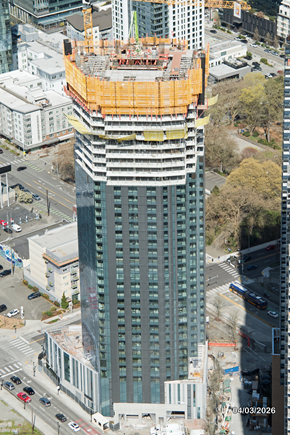 Aerial view of a tall building under construction with a partially completed top and surrounding urban landscape.
