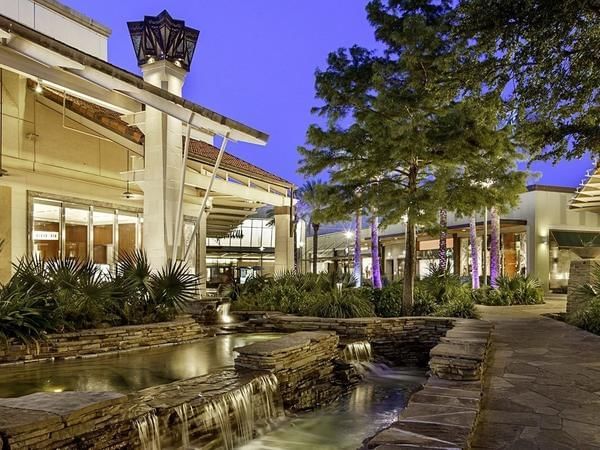 A beautifully landscaped outdoor community area featuring a water feature and greenery, illuminated by soft lighting in the evening sky.