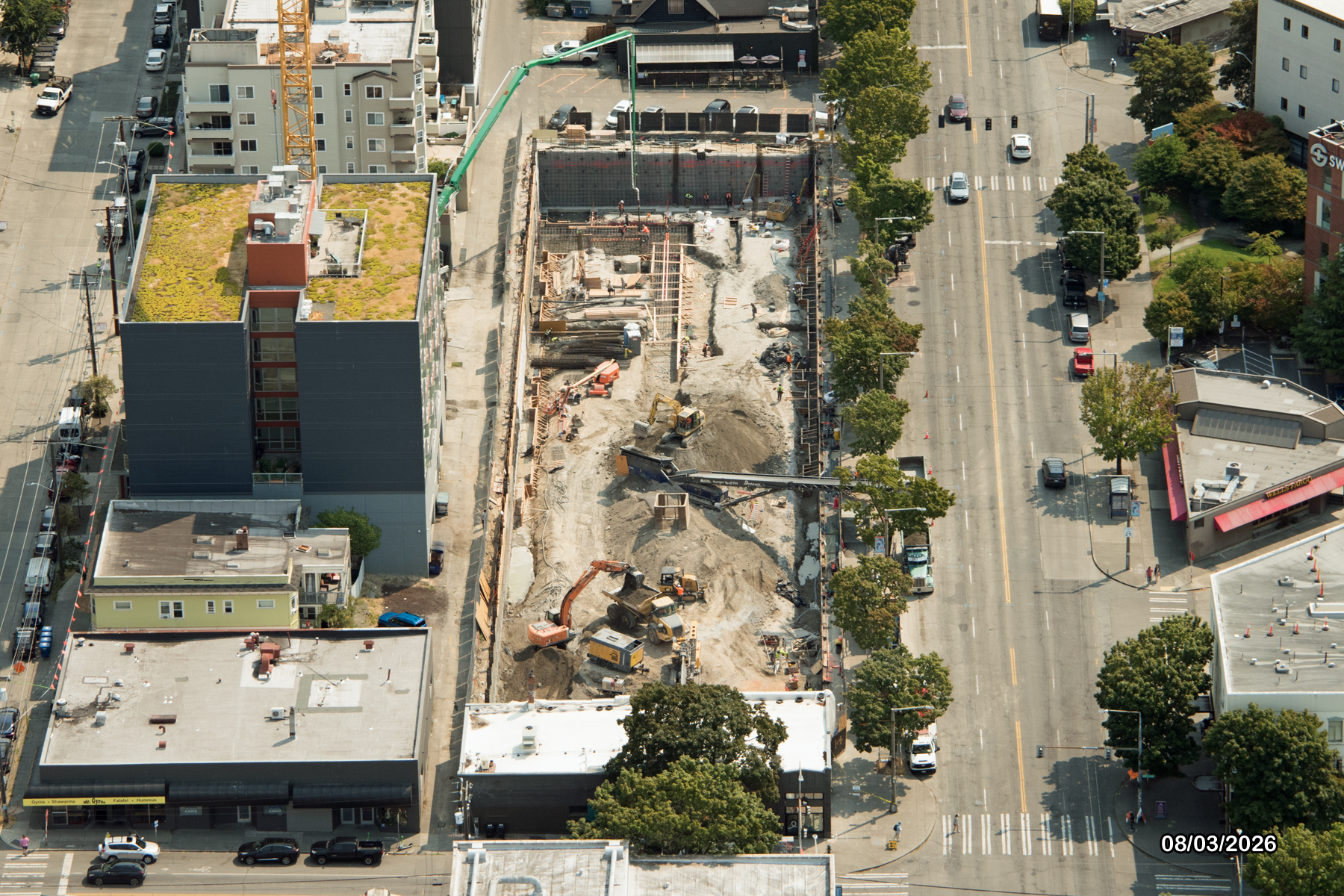 Aerial view of a construction site with machinery and building materials, surrounded by city streets and buildings.