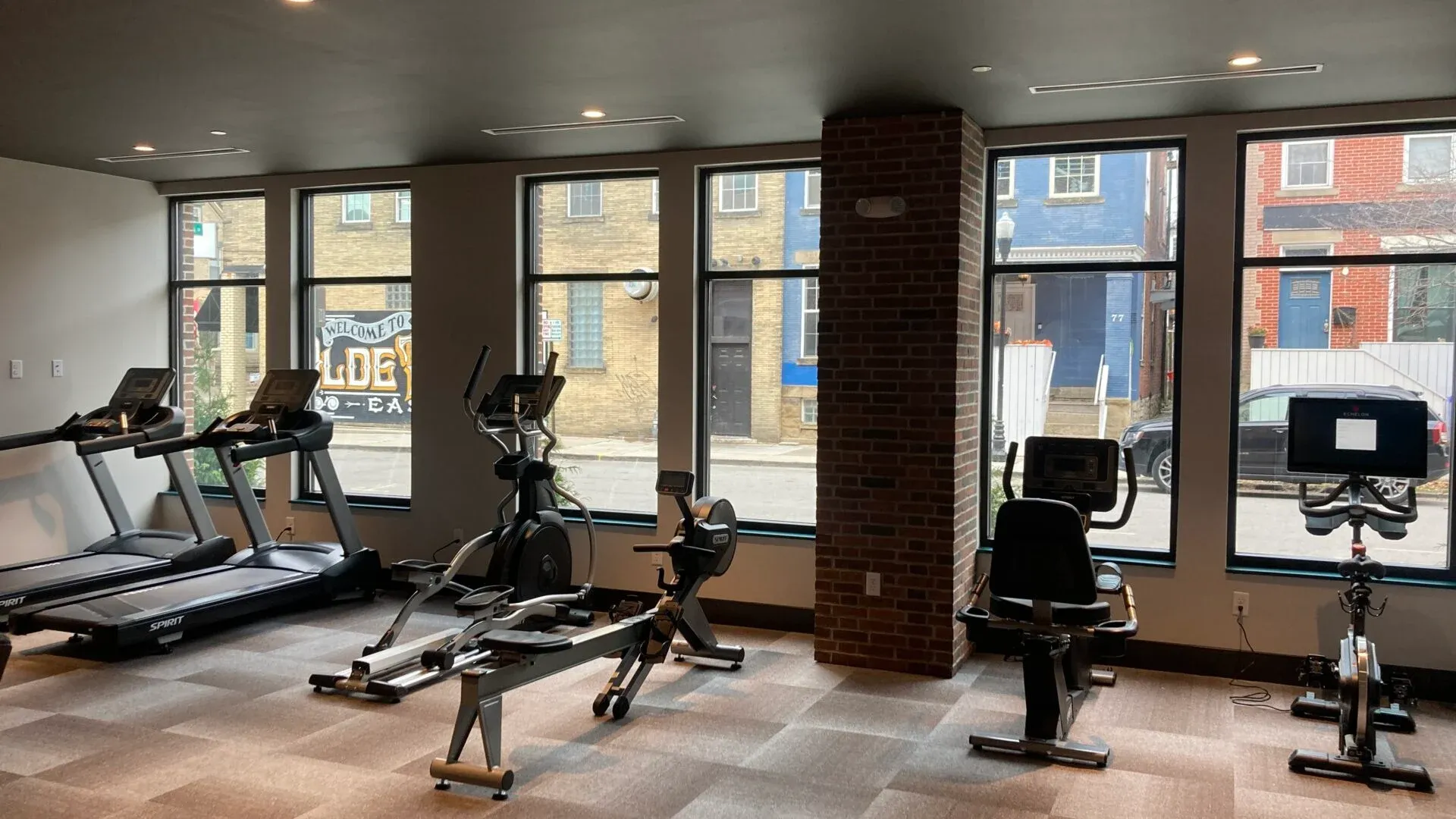 A shared gym space featuring treadmills, ellipticals, and stationary bikes with large windows providing views to the outside.
