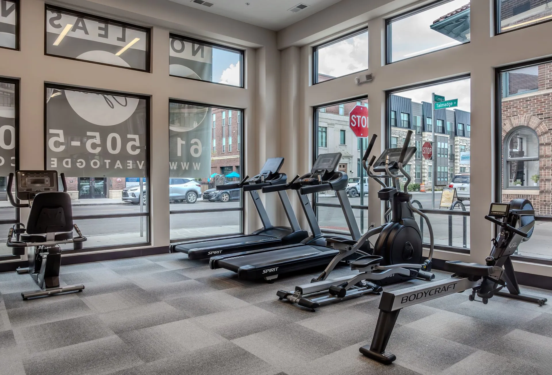 Interior view of a modern gym with cardio equipment, large windows, and a clean floor.