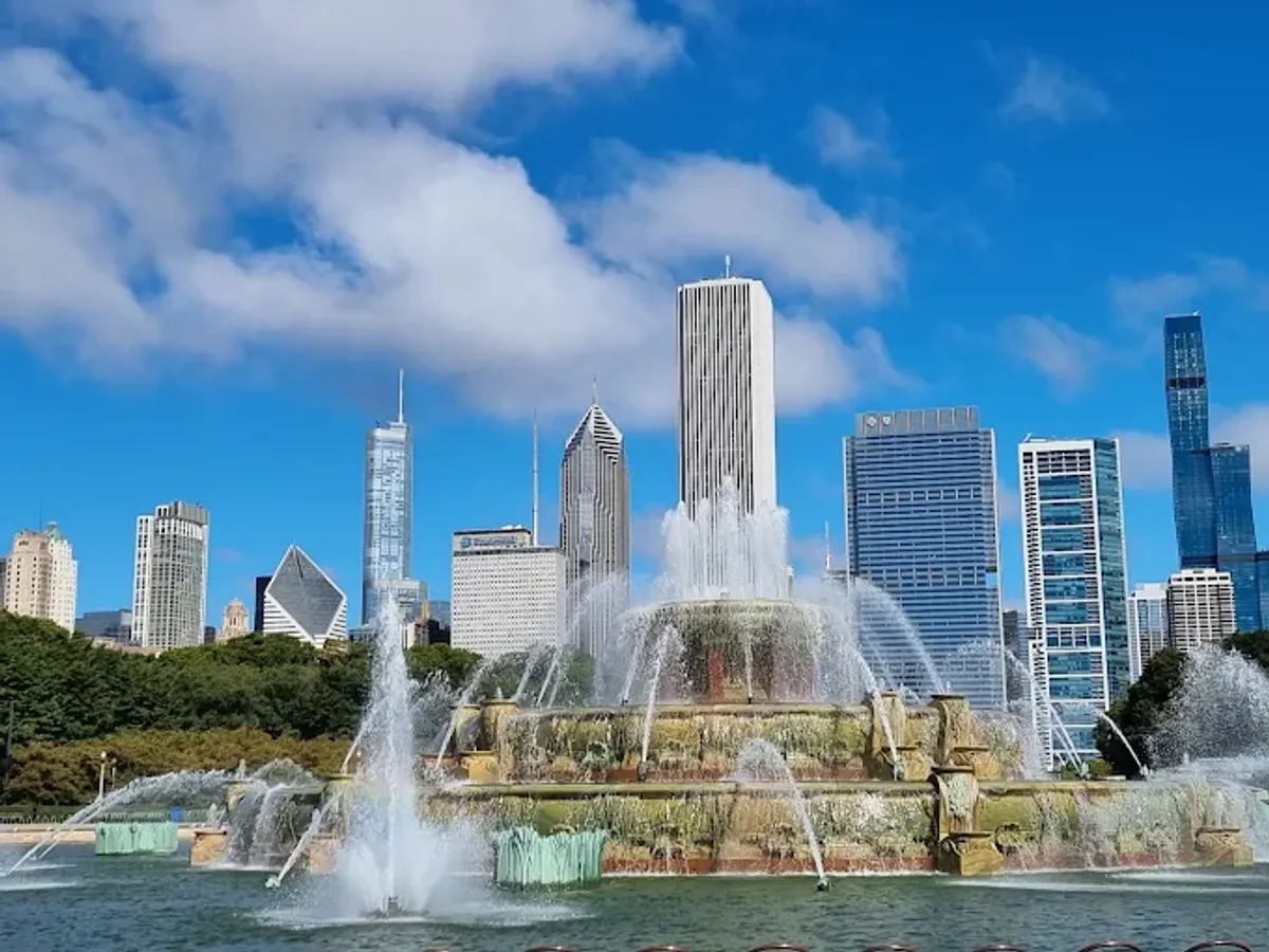 A view of Buckingham Fountain in Chicago with a backdrop of modern skyscrapers and a blue sky with fluffy white clouds.
