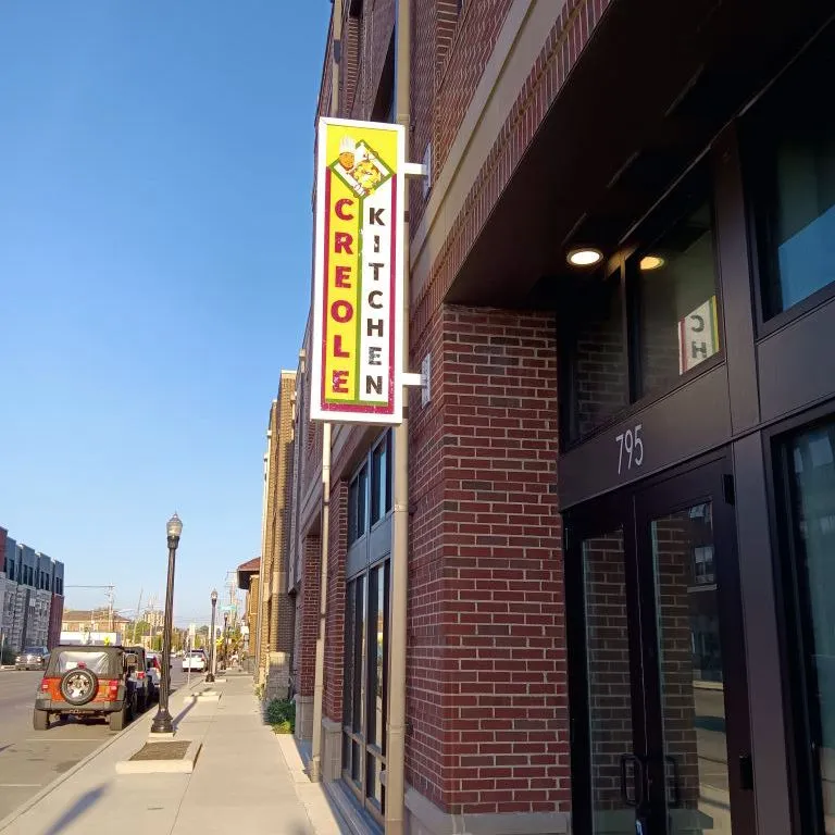 A red brick building with a sign that reads 'CREOLE KITCHEN' attached to the wall, next to a sidewalk.