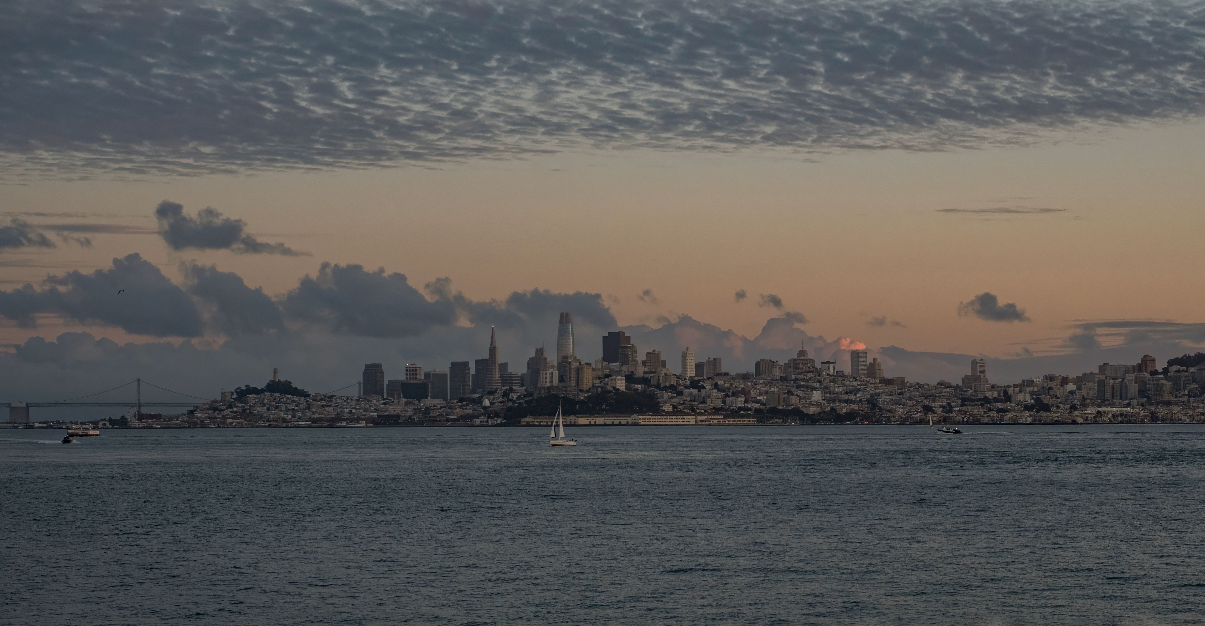 A wide view of the San Francisco skyline at sunset, featuring various buildings against a colorful sky and gentle waves in the foreground.