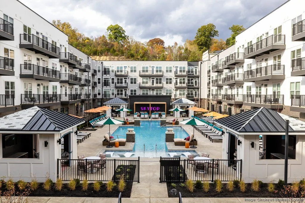 A view of a community pool area surrounded by modern apartment buildings with lounge chairs and cabanas.