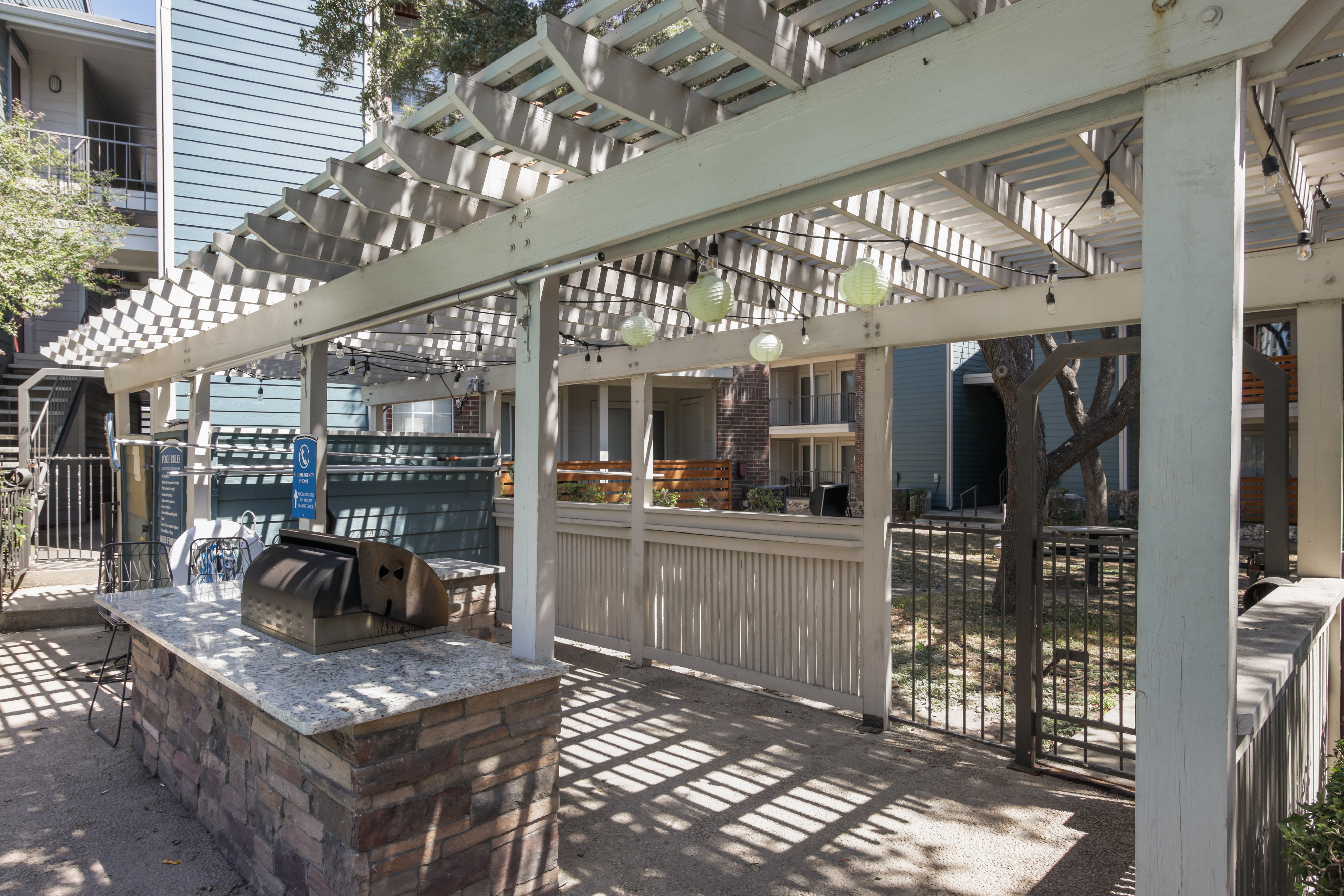 An outdoor grilling area with a shaded pergola, stone countertop, and string lights.
