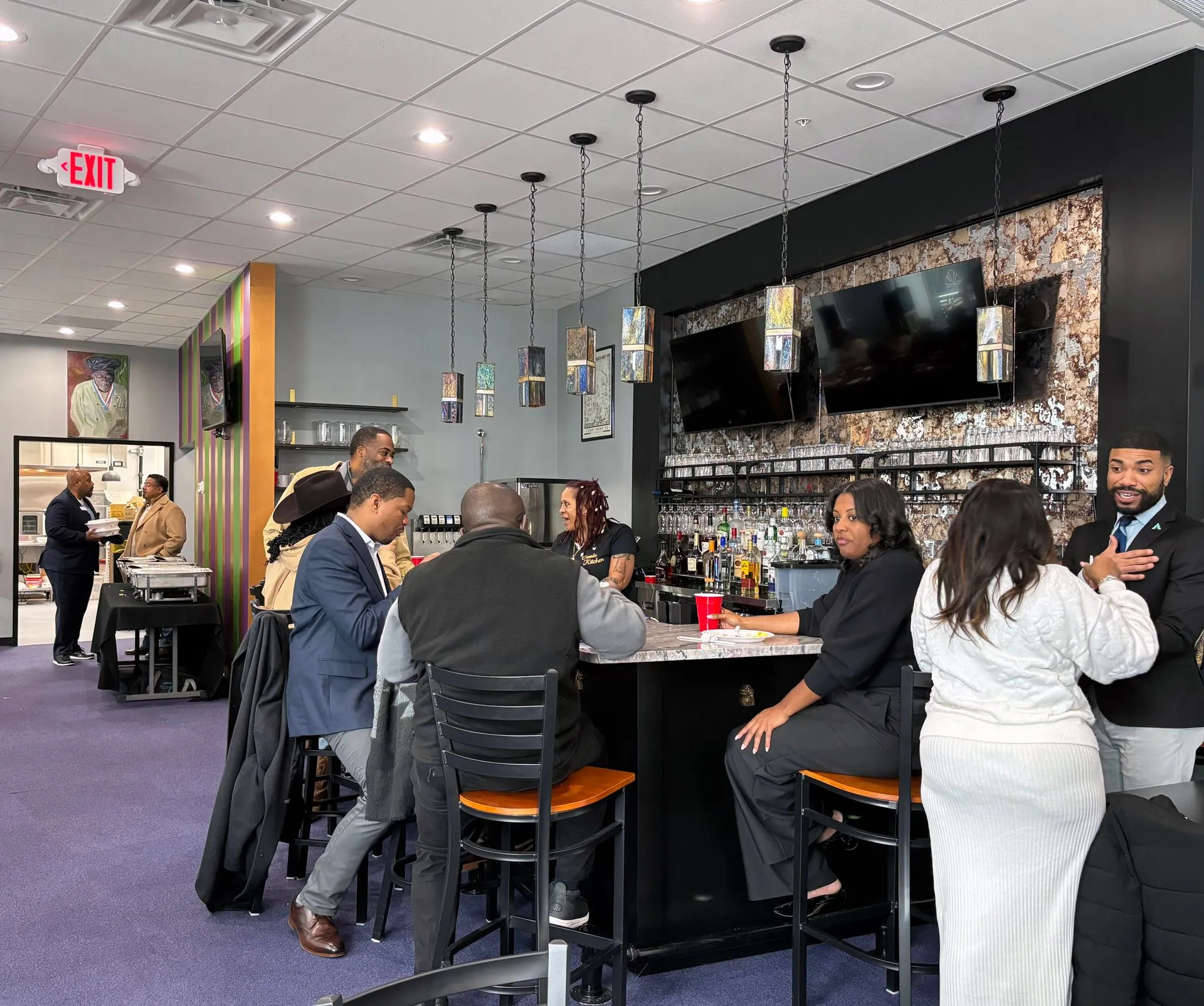 A lively bar scene featuring diverse patrons engaging in conversation and enjoying beverages. The interior is modern, with a well-stocked bar and hanging lights.