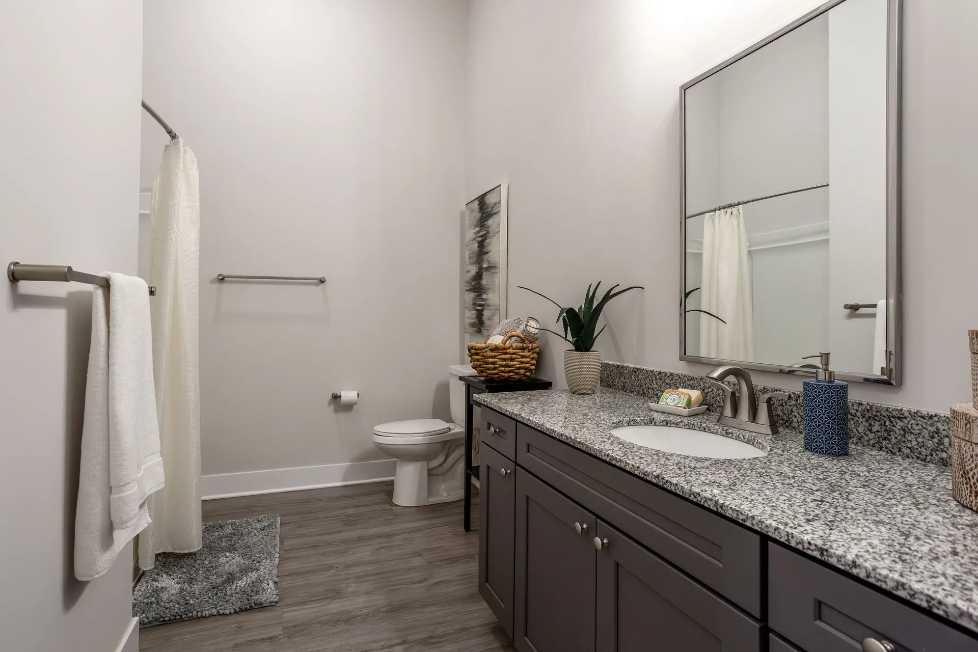 A modern bathroom featuring a large mirror, granite countertop, and neutral colors.