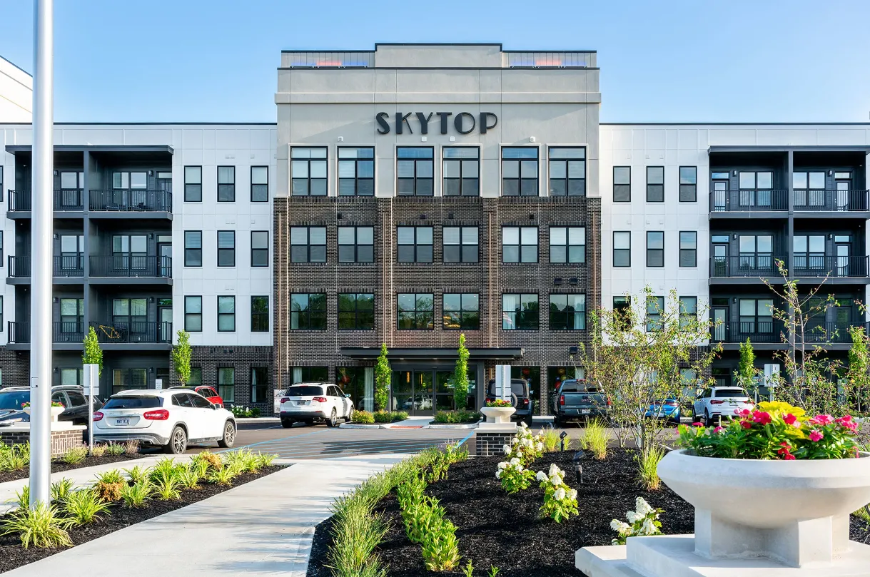 Exterior view of a modern apartment building named Skytop with landscaped grounds and parking area.