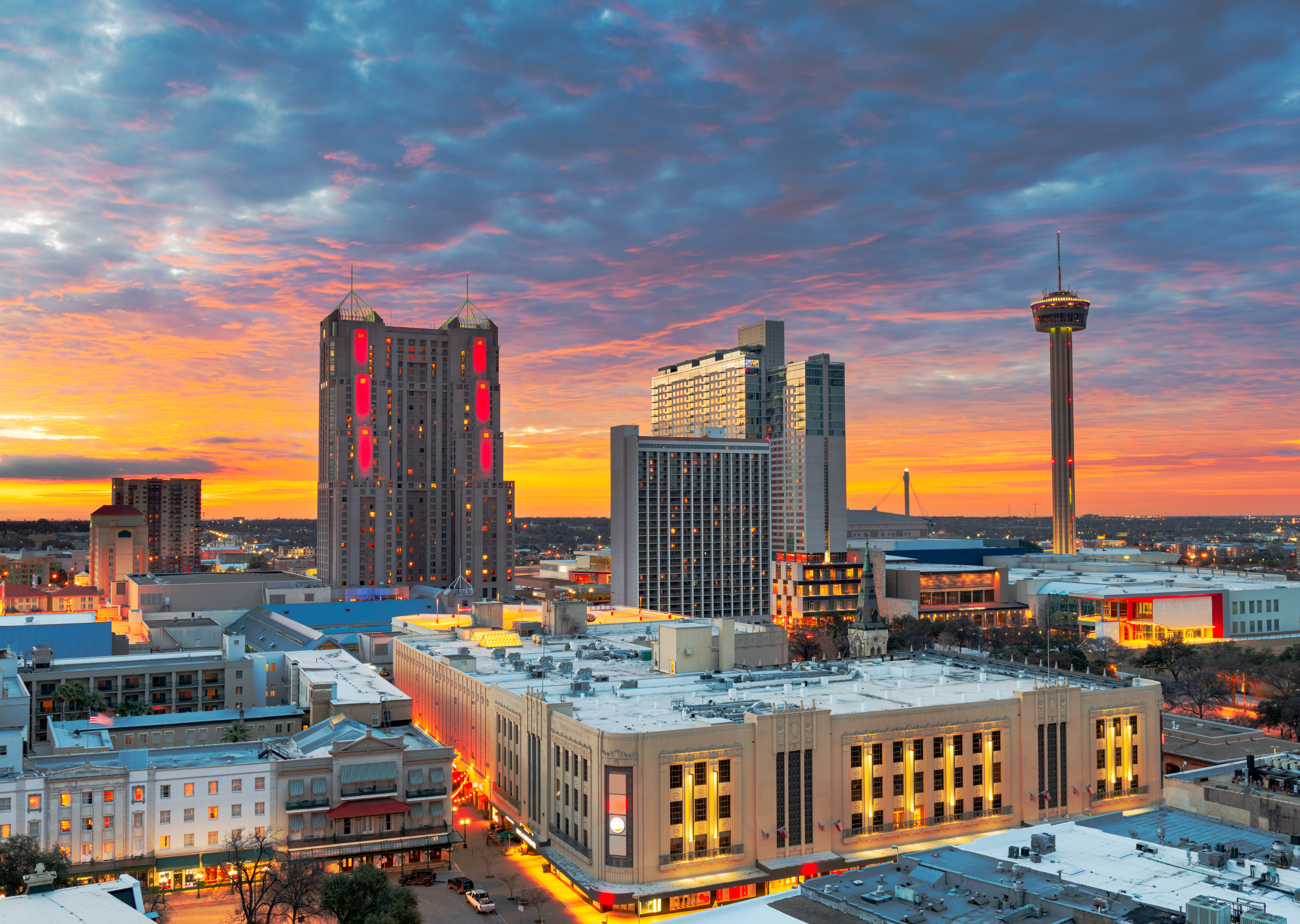 A vibrant skyline view of San Antonio at sunset, featuring modern buildings and the iconic Tower Life Building.