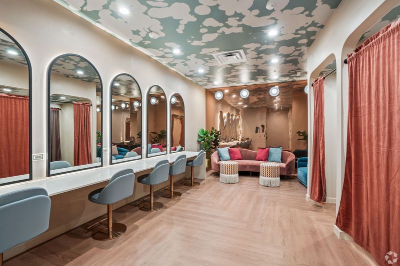 A stylish community lounge area featuring multiple mirrors, plush seating, and decorative ceiling. The room has a modern aesthetic with soft lighting and potted plants.