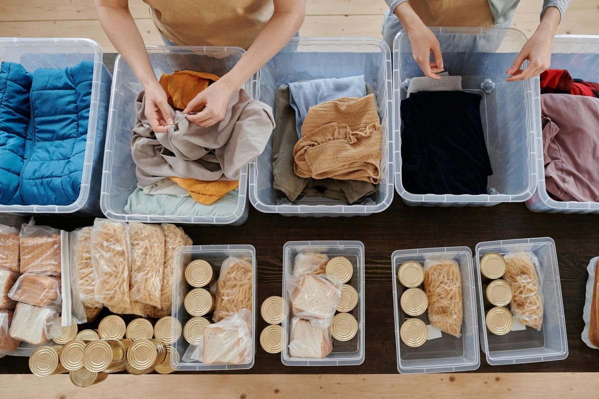 Two people sorting clothes and packaged food items in opaque containers on a wooden table.