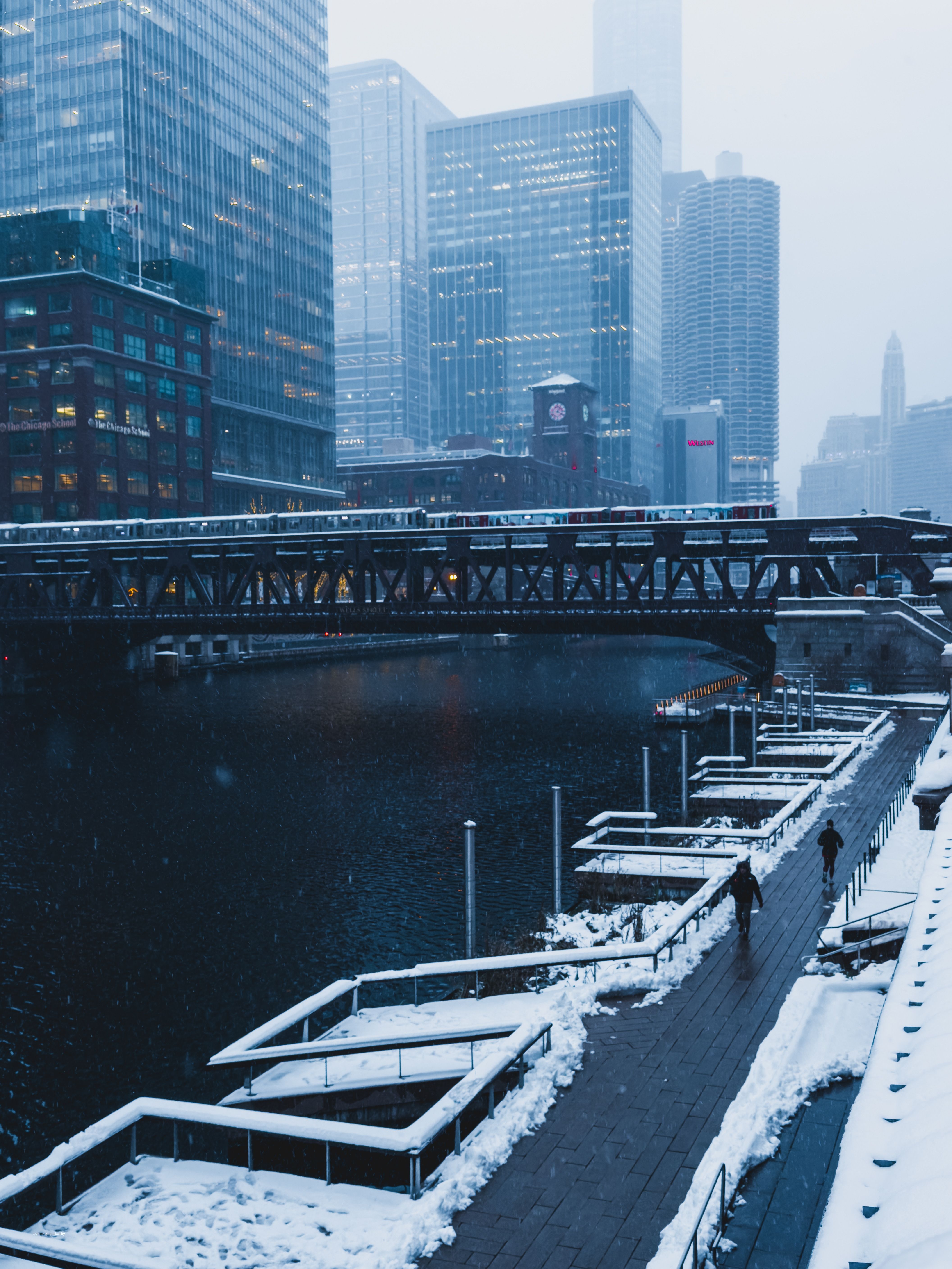 Snow-covered urban scene with a river and buildings in the background.