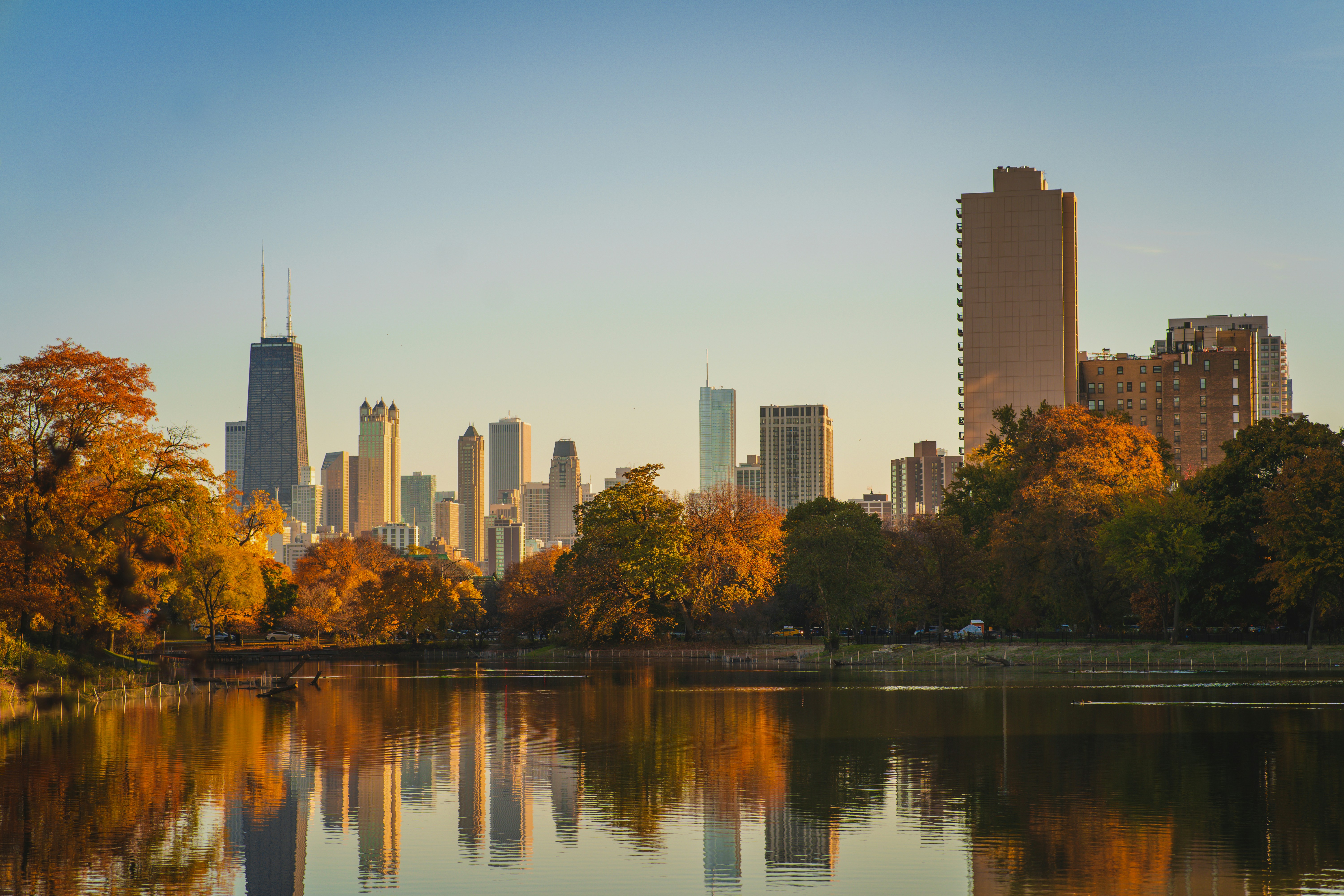 A city skyline with colorful autumn foliage and a serene lake reflecting the buildings.