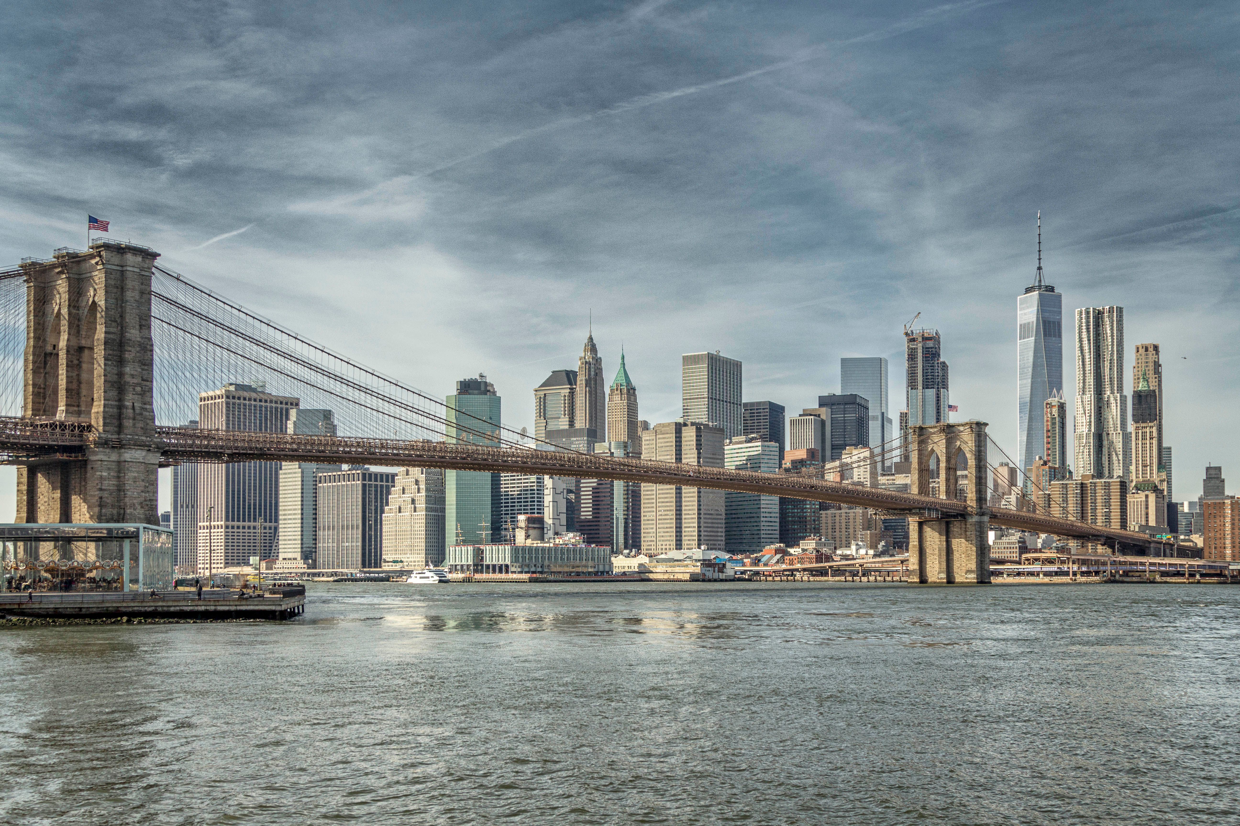 A scenic view of the Brooklyn Bridge with the New York City skyline in the background, featuring skyscrapers and a calm river.