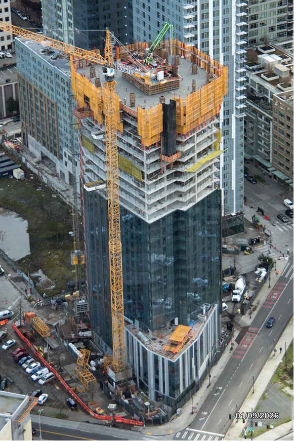 Aerial view of a high-rise building under construction with cranes and scaffolding.