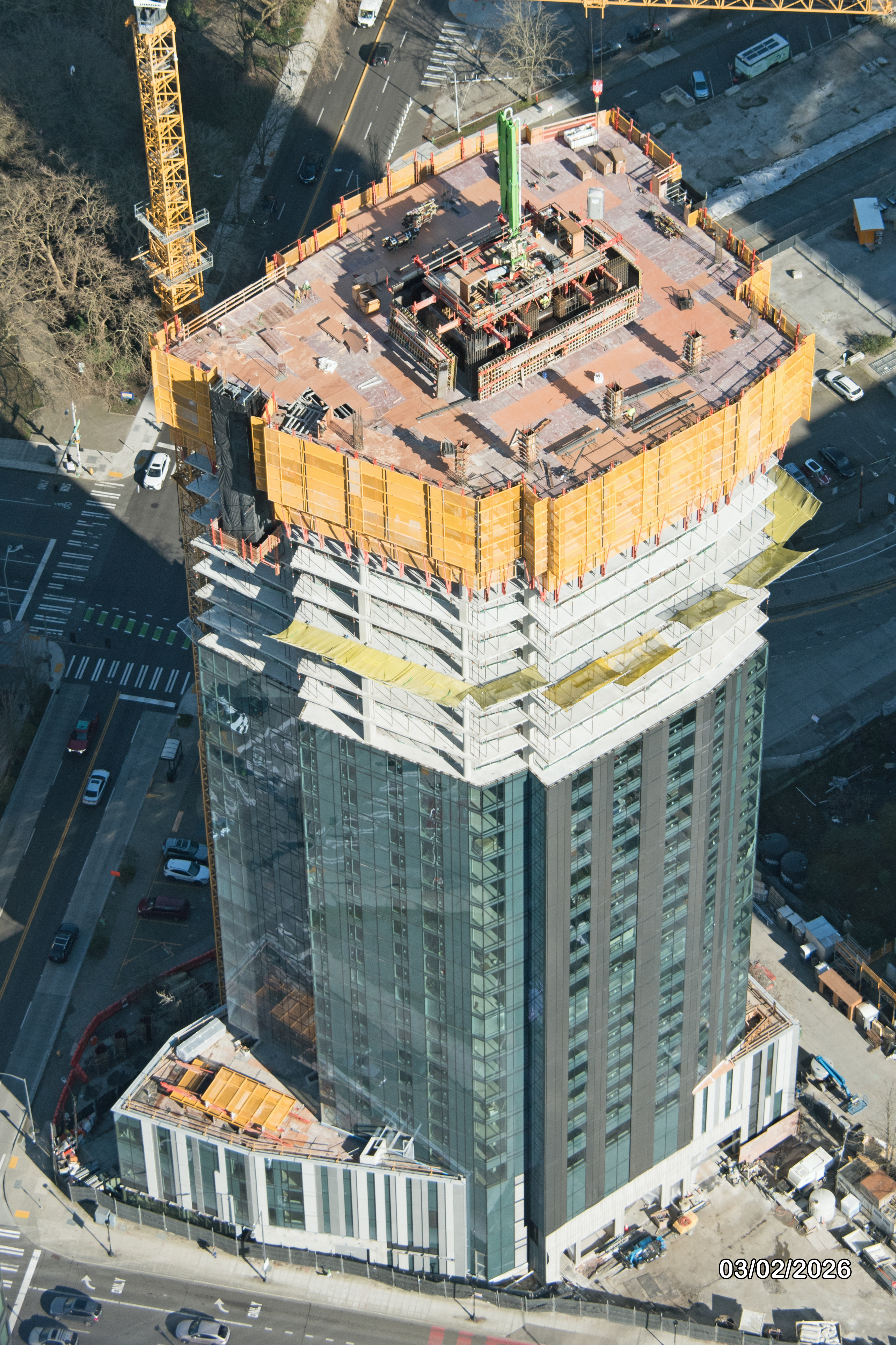 Aerial view of a skyscraper under construction, showcasing the building's top with cranes and scaffolding.