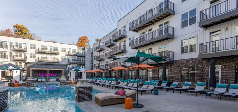 A modern apartment complex featuring a swimming pool with lounge chairs and umbrellas.
