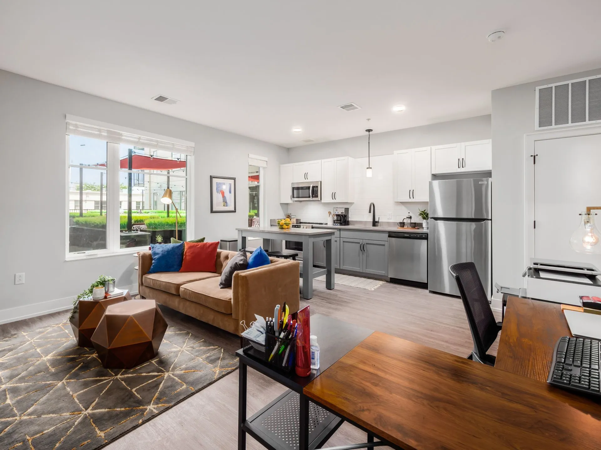 An open-plan living space featuring a cozy couch, a kitchen with modern appliances, and a workspace with a desk.
