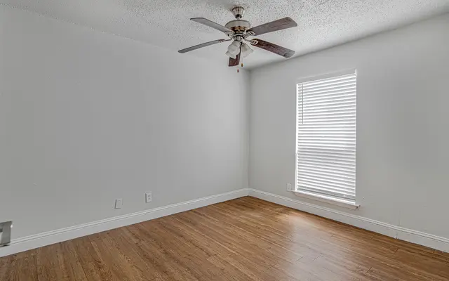 Unfurnished room with wood flooring, white walls, ceiling fan, and window.