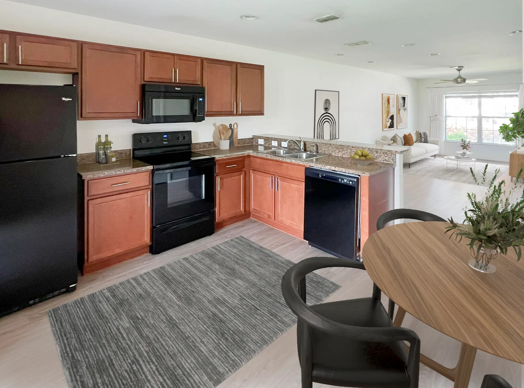 Modern kitchen with dark wood cabinets, black appliances, and a dining table on a rug, leading to a bright living area.