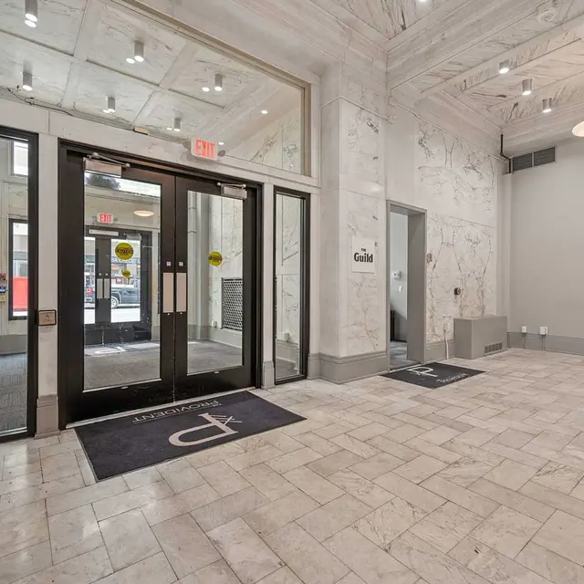 Spacious lobby with marble floors, high ceiling, glass entrance doors, and welcome mats on the floor.