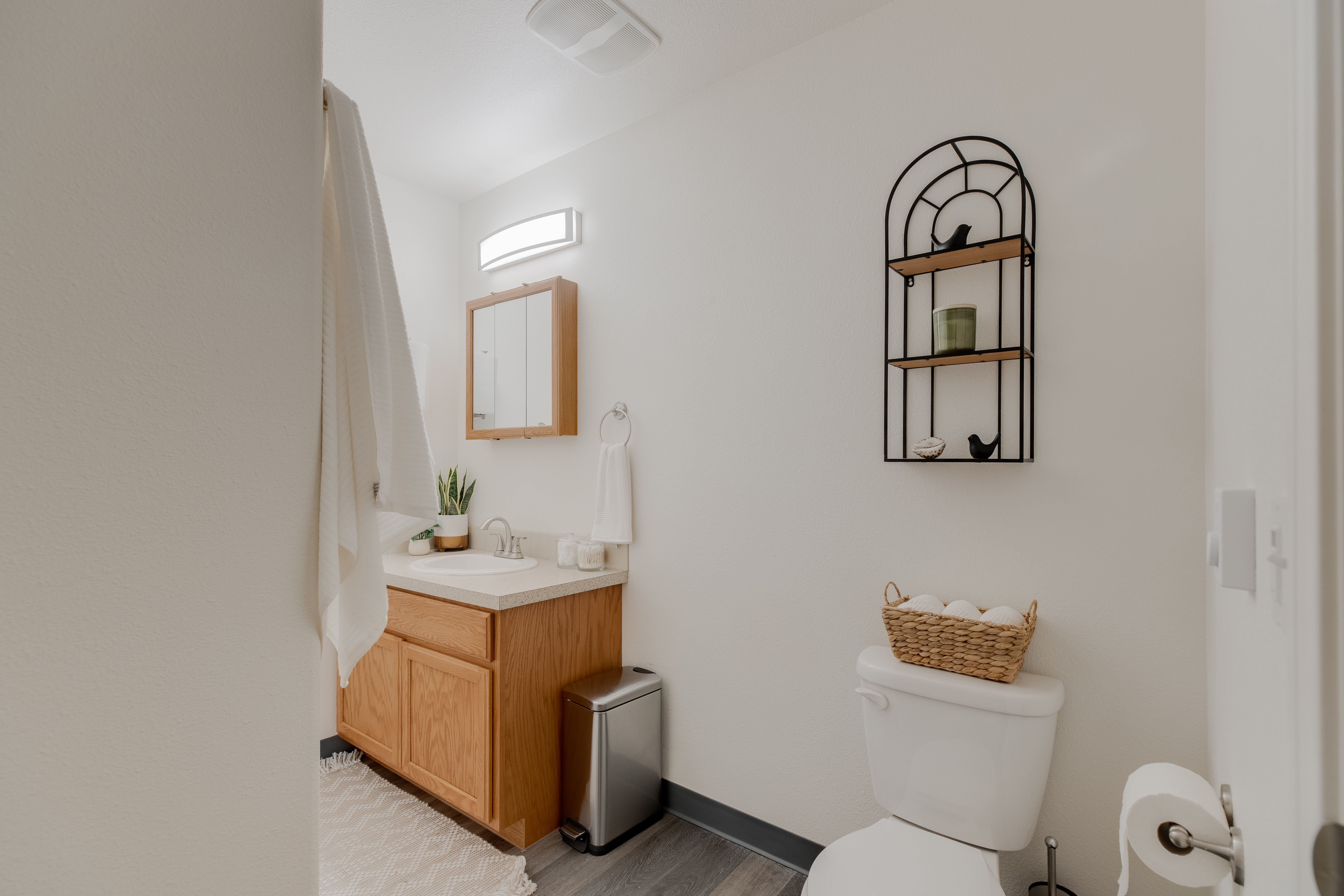 Modern apartment bathroom at The Landing at Clearwater in Moscow, Idaho, featuring a wood vanity, built-in mirror, stylish wall shelf, woven storage basket, and soft lighting. A neutral color palette and minimalist decor create a clean and inviting space.

