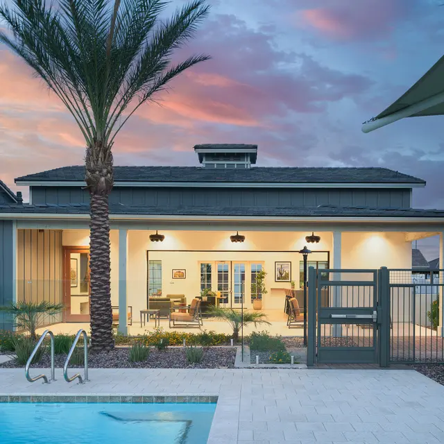 Modern home with a pool and palm trees, featuring a spacious patio and dusk sky with colorful clouds in the background.