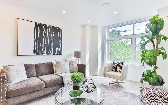 Modern living room with a brown sofa, a glass coffee table, a large black-and-white artwork, and a potted plant by the window.