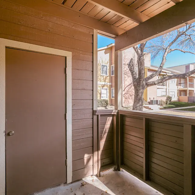 A view from a porch looking towards a doorway and an apartment complex with trees and clear blue sky.