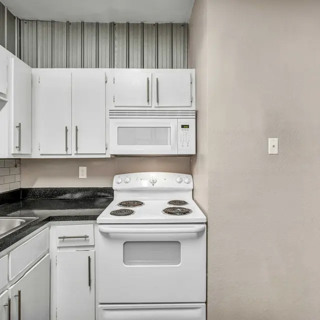 A kitchen corner with white cabinets, white appliances, white subway tile backsplash, and a double basin sink near a hallway.