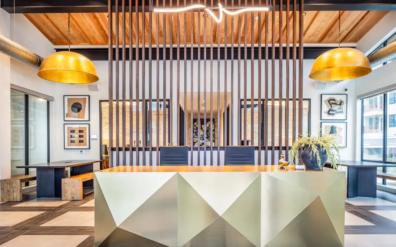 A lobby with a desk and two chairs, and light fixtures hanging from the ceiling.