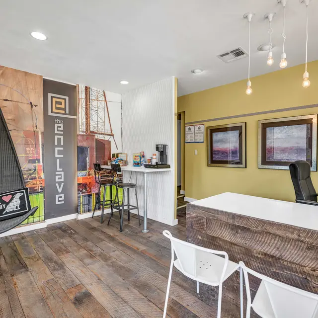 The Enclave's leasing office with an L-shaped desk, chairs, hanging lights, a hanging chair, and 2 stools at a desk.