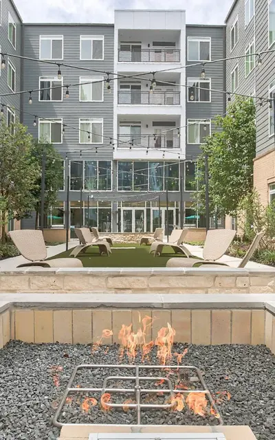 Courtyard fire pit area with lounge chairs, set in front of 120 Ninth Street Apartments featuring balconies and large windows.