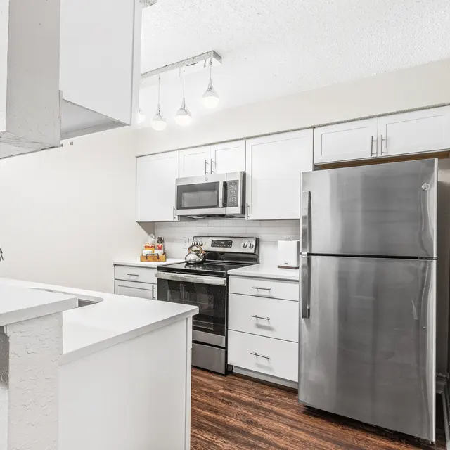 Kitchen with overhanging lights, stainless steel appliances, white cabinets, and hardwood-style floors.