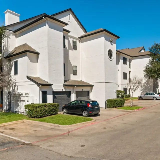 Arboretum at Lewisville exterior with private garages, apartment entrances, and parked vehicles in Lewisville, TX.