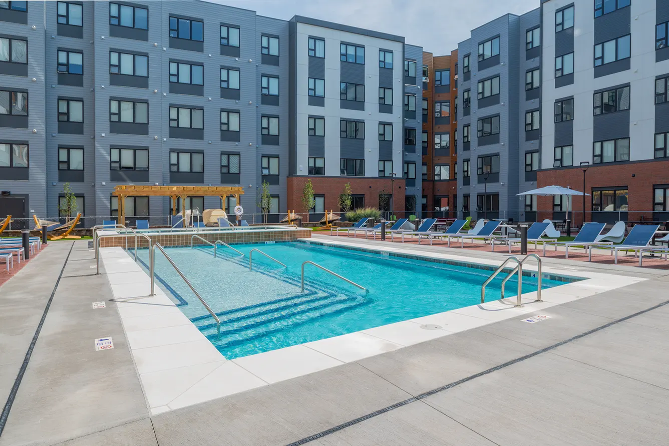 Apex Fully Furnished Student Apartments In Henrietta, NY - APEX - Resort-Style Pool With Dual Hot Tubs, Spacious Sundeck, Lounge Chairs, Umbrellas, And Hammocks.