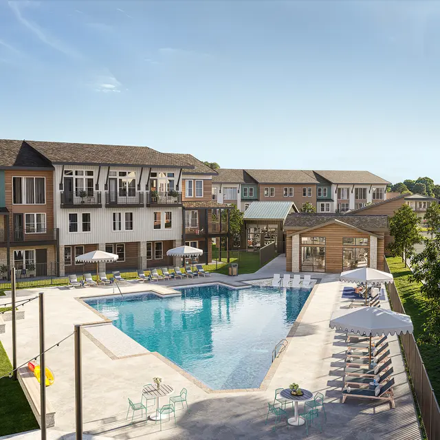 A view of an apartment complex featuring a large swimming pool surrounded by lounge chairs and umbrellas. The complex includes multiple buildings with balconies and landscaped areas with grass.