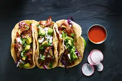 Three tacos on plate with salsas