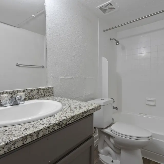 A clean and modern bathroom featuring a granite countertop sink, a mirror, a bathtub, and a toilet.