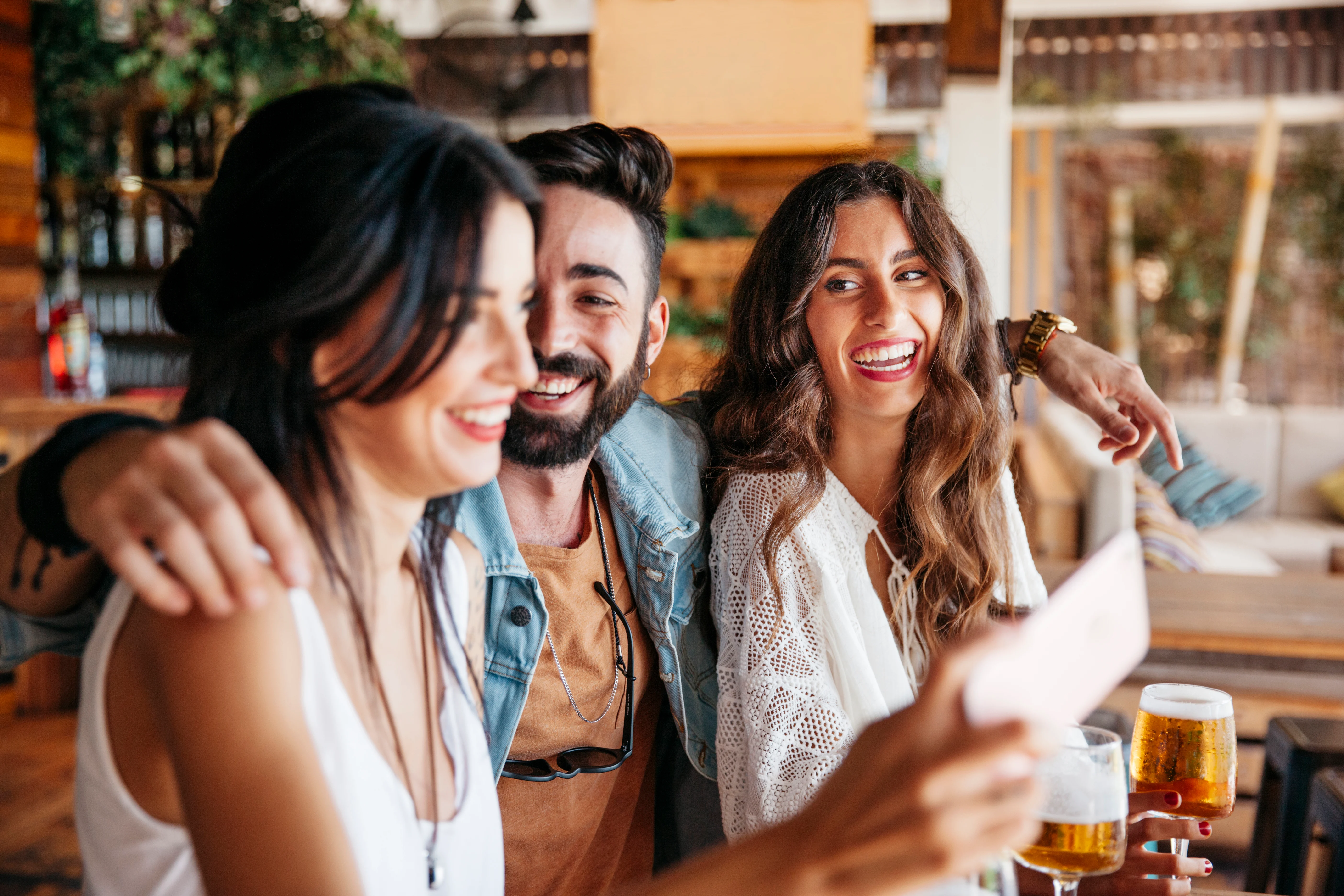 Friends Taking a Selfie at a Bar Three friends laughing and taking a selfie at a bar, with drinks in front of them.