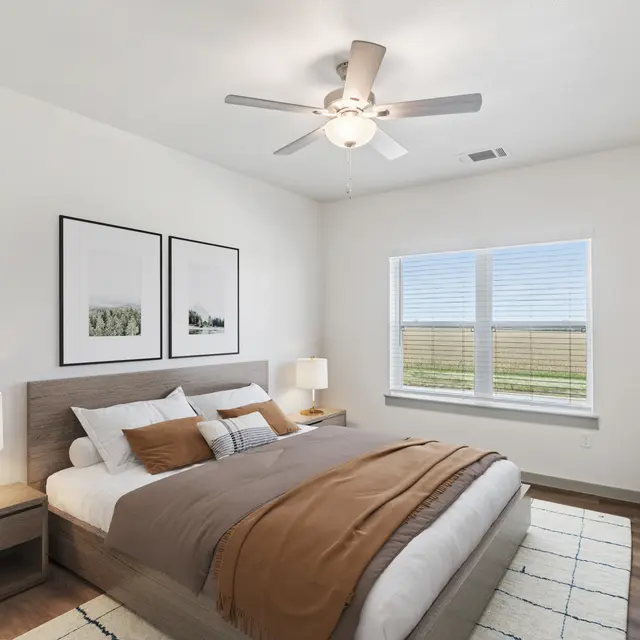 A modern bedroom featuring a bed with brown and white bedding, two bedside lamps, and artwork on the walls. A window allows natural light in, with a view of greenery outside.