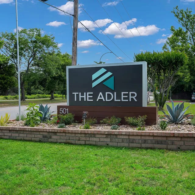 Sign for 'The Adler' with lush greenery and clear blue sky in the background.